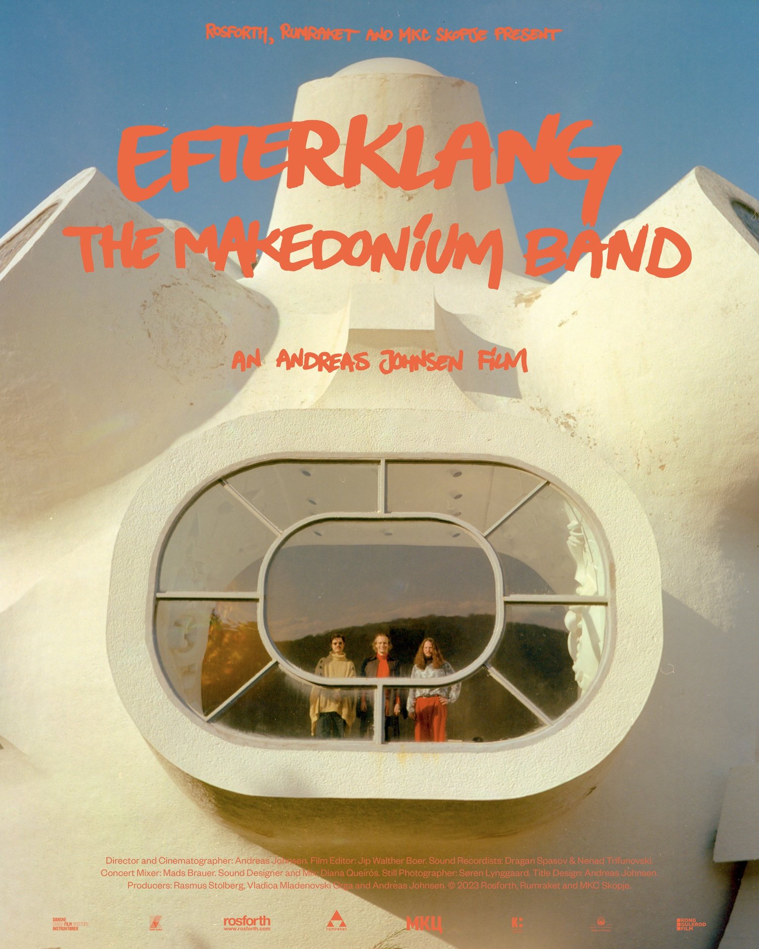 Film poster for Efterklang: The Makedonium Band — the trio seen through the oval window of the white concrete Makedonium monument