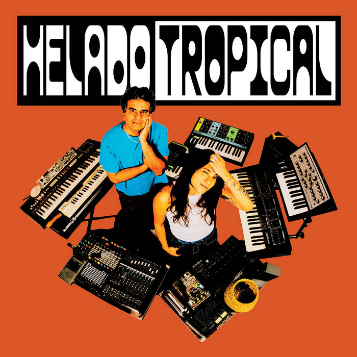 Helado Tropical album cover — the two collaborators seen from above on an orange floor, ringed by keyboards, synths, and a drum machine