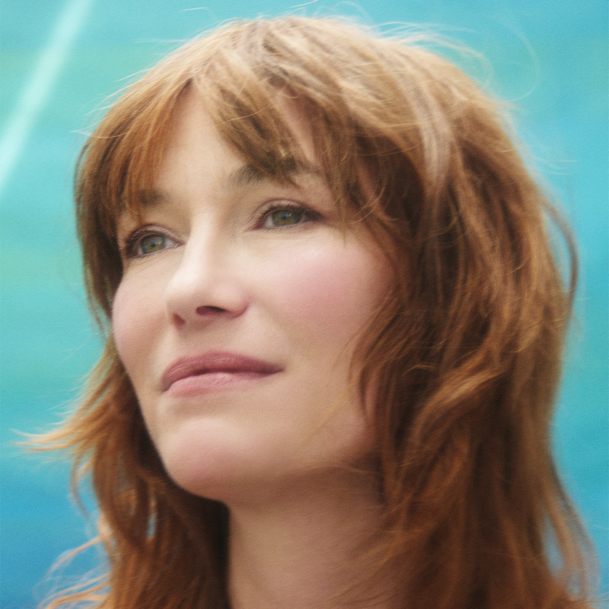 Mina Tindle — close portrait, red-brown fringe, looking off to the left against a turquoise-blue ground