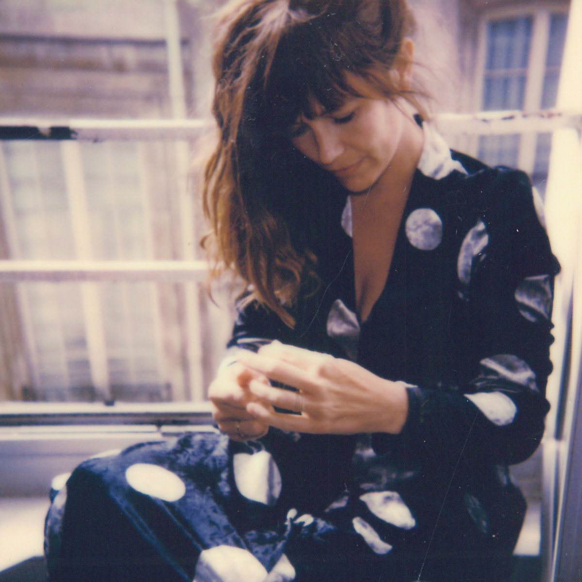SISTER album cover — Polaroid-style photo of the artist seated in a window in a dark dress printed with pale moons, looking down at her hands